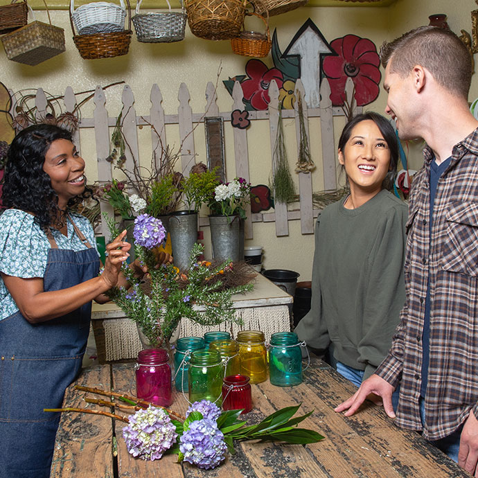 A female flower shop owner protected under TruStage Specialty Commercial Program insurance creates a floral arrangement for a smiling couple.