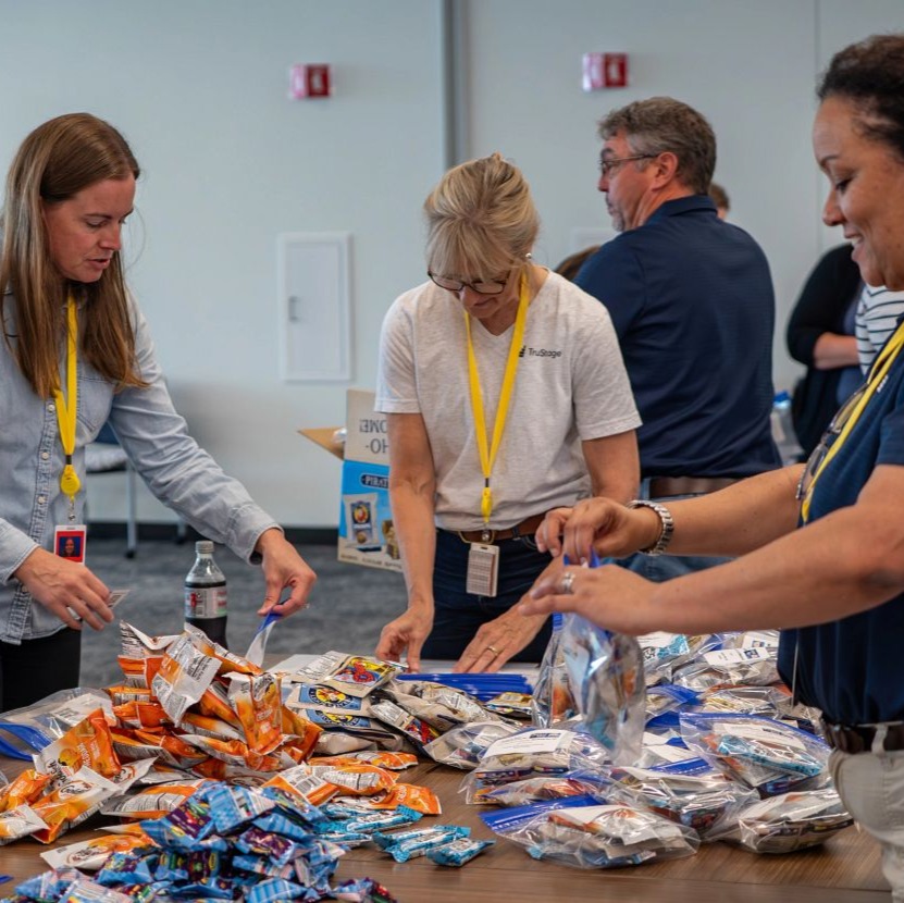 Three TruStage women packing snacks for students.