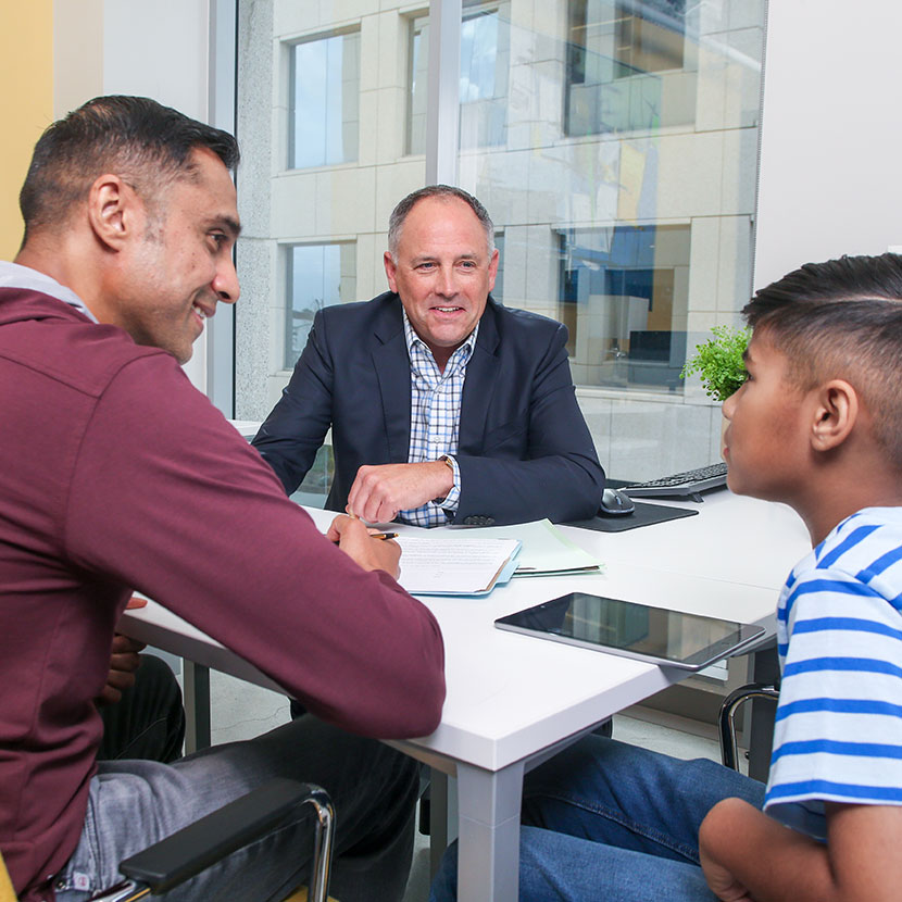 A father and son sit at a desk with a financial professional discussing the commitment TruStage has made to credit unions.