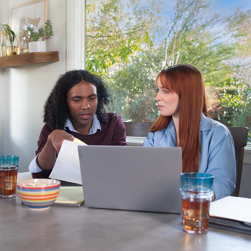 Two young adults sitting at a table with a laptop discussing TruStage Payment Guard Advantage