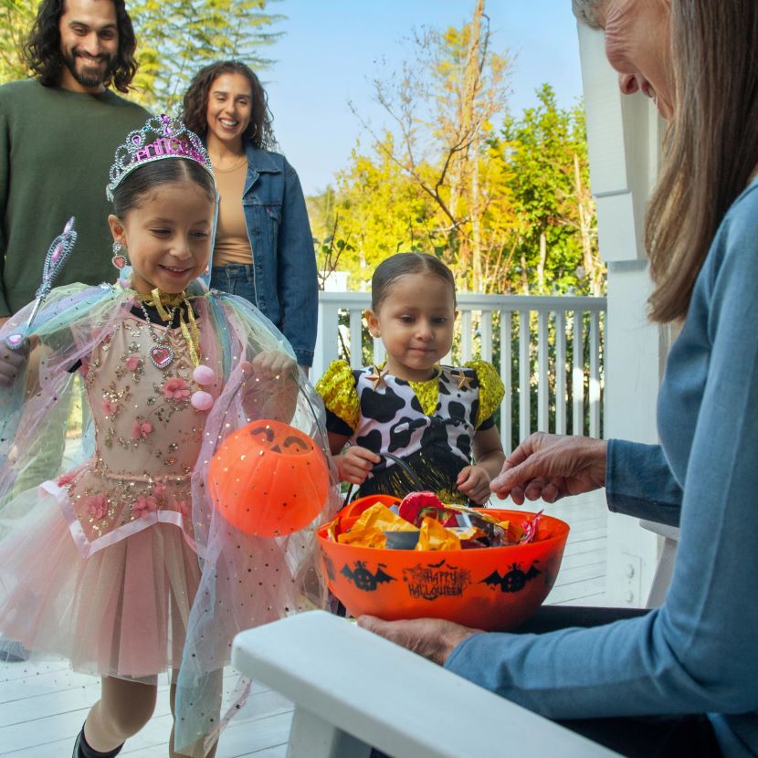 A woman sits on her front porch and gives out candy to two children on Halloween.