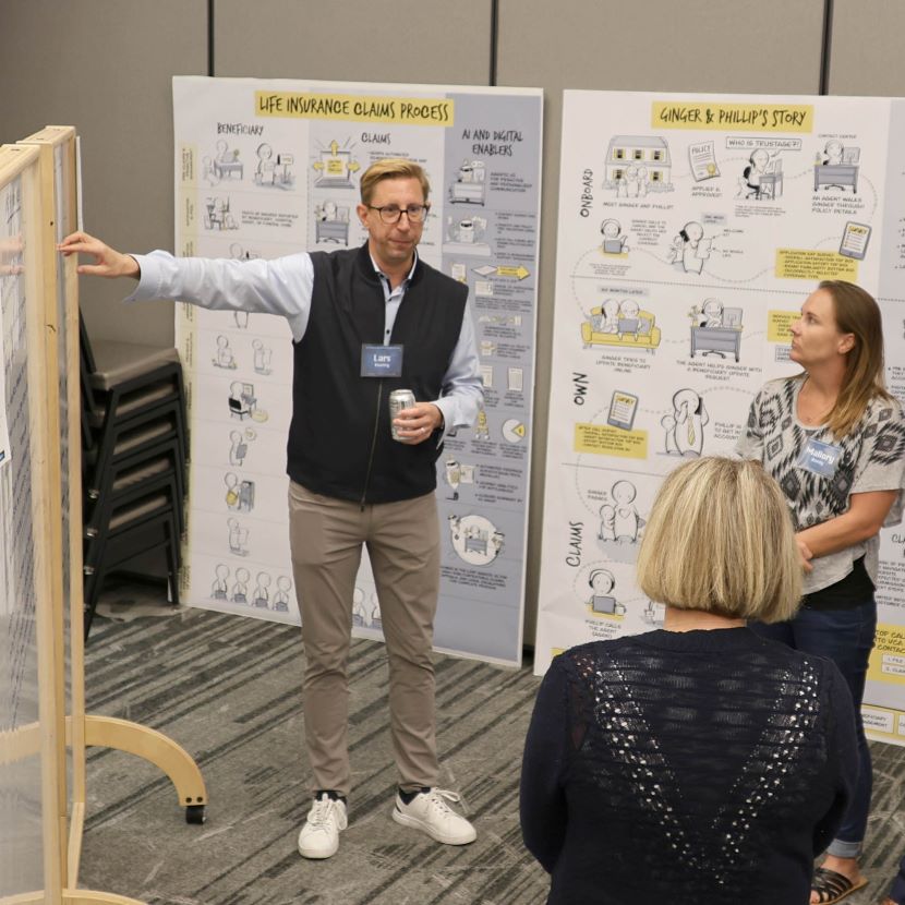 A man points at a wall displaying research as he stands in front of other financial professionals.