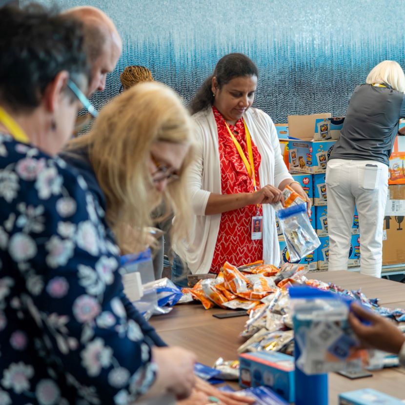 TruStage employees gather around a table as they pack snacks for students.
