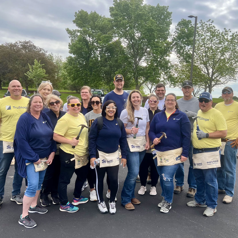 TruStage team members stand together holding hammers as they roll up their sleeves to help Habitat for Humanity.
