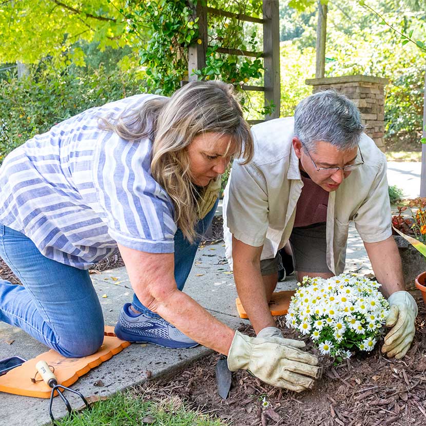 A retired couple plants flowers and feels secure about retirement, thanks to a registered index-linked annuity from TruStage™.