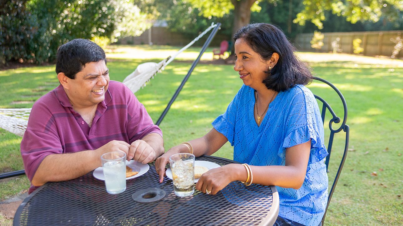 Man laughing and woman looking at something out of frame, sitting outside at a table