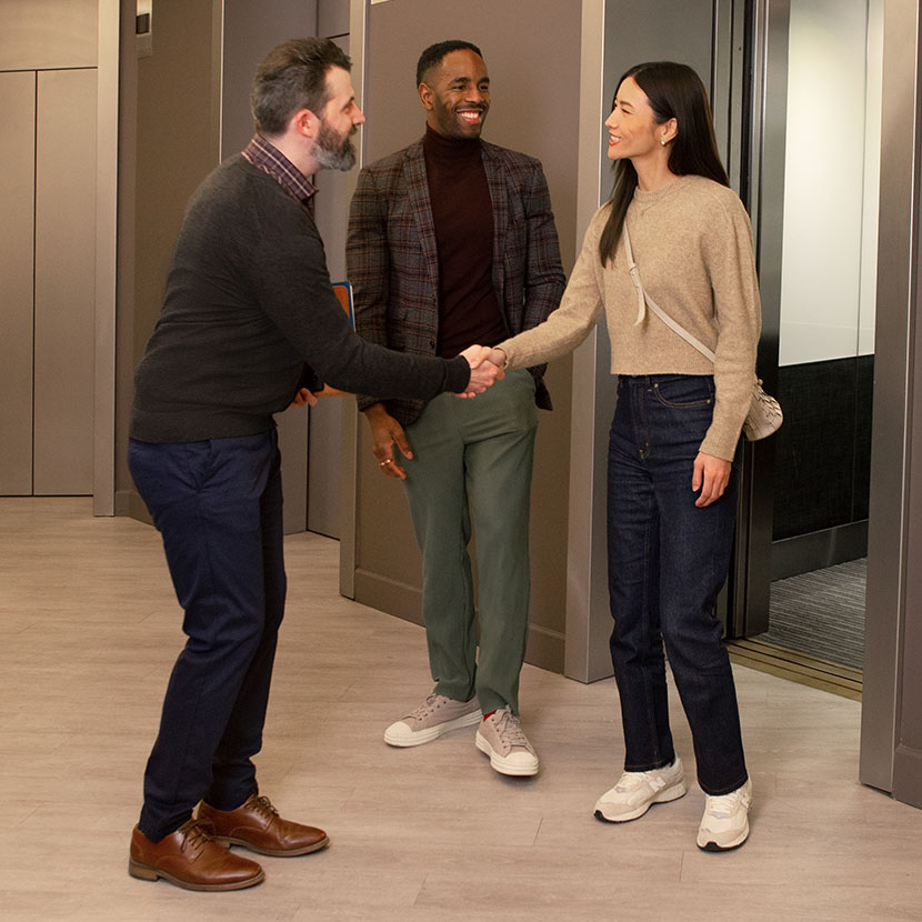A financial professional warmly greets two clients interested in TruStage Annuities as they get off the elevator.