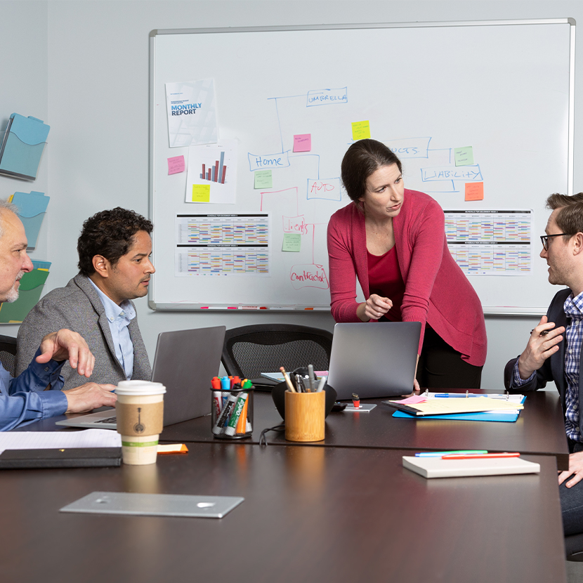 Group of people in an office setting, all around a table, talking.