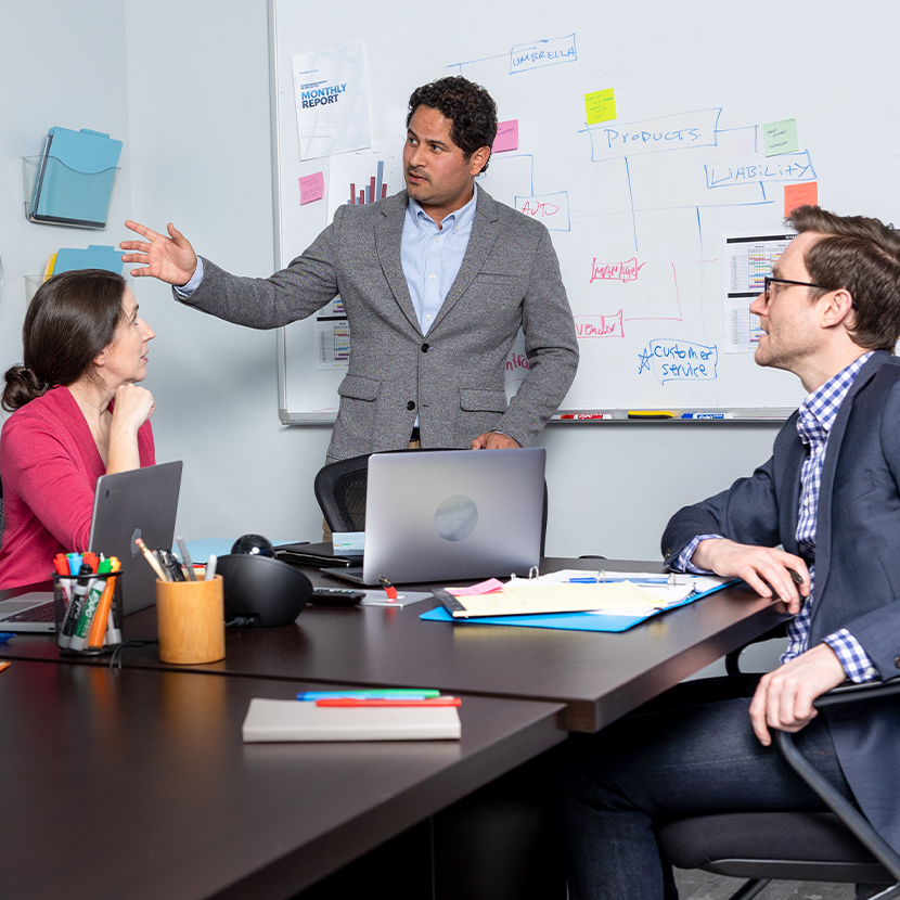 Group of people in an office setting, all around a table, talking.
