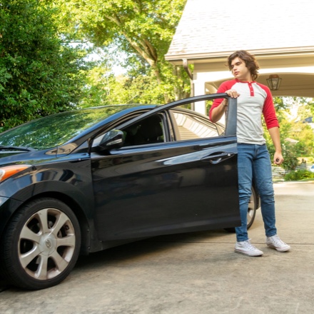 A student driver about to enter his car is protected with auto insurance.