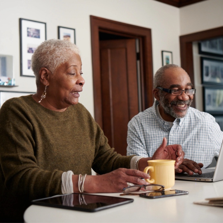 A couple uses their laptop at the dining table to review their policy insurance online