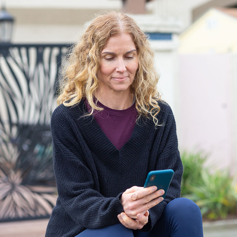 A woman sits outside and views TruStage payment protection offers on her phone.