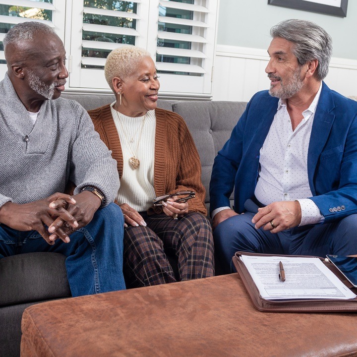 A husband and wife sit on a couch with a financial professional to discuss the importance of burial insurance.