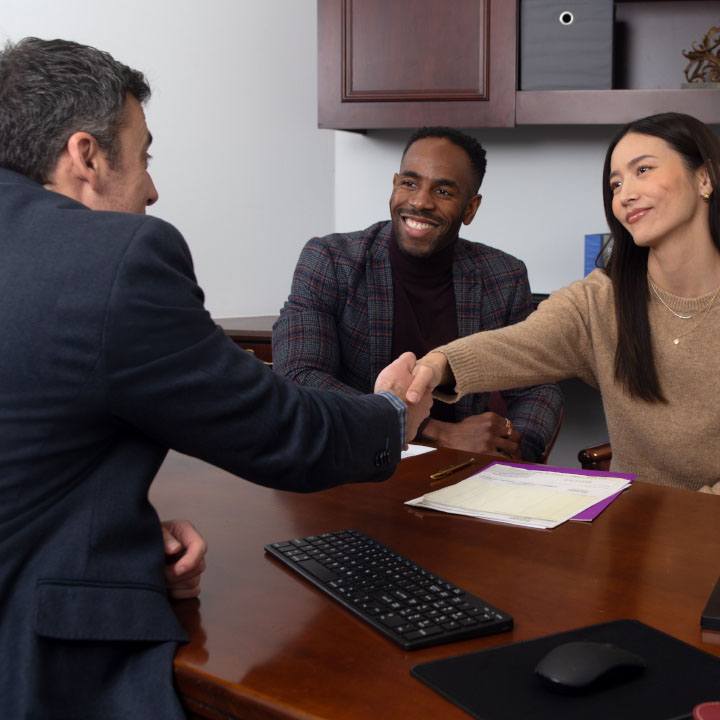 A husband and wife sit at a desk and shake hands with a financial professional.