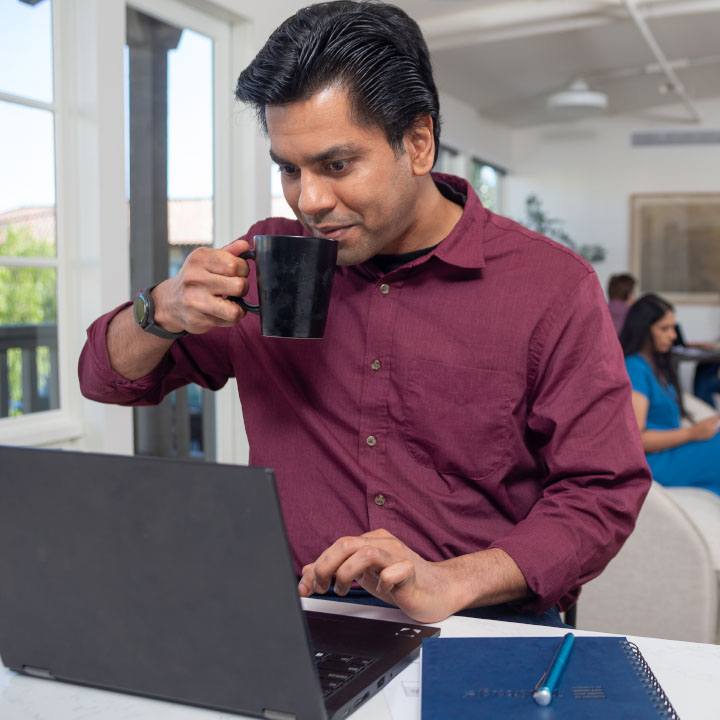 A man sips his coffee while browsing for car insurance online using his laptop.