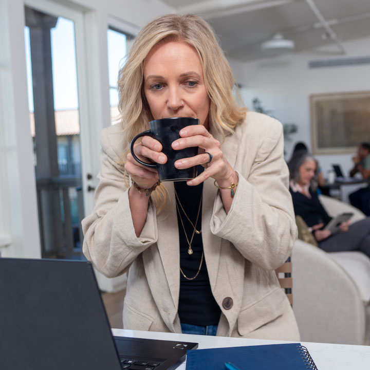 A woman sips coffee while reading about high inflation on her laptop.