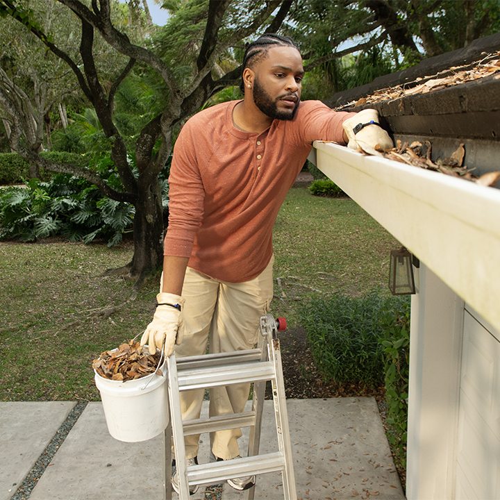 A man cleaning out gutters at his house