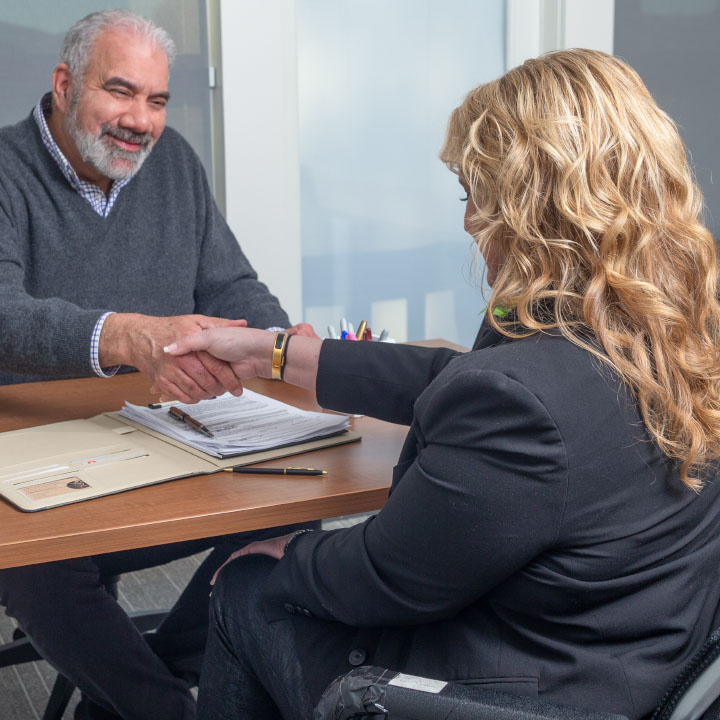 A man and woman sit at a desk and shake hands after discussing the importance of life insurance.