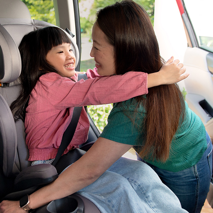 A mother hugging her child sitting in the backseat