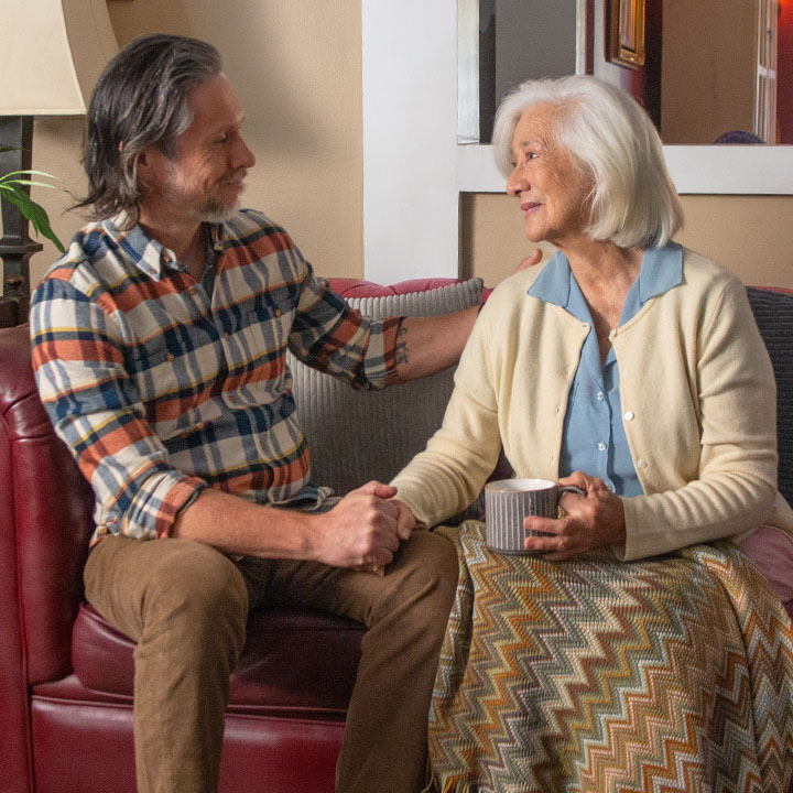An elder mom and adult son are on a couch discussing a family member's TruStage Life Insurance claim.