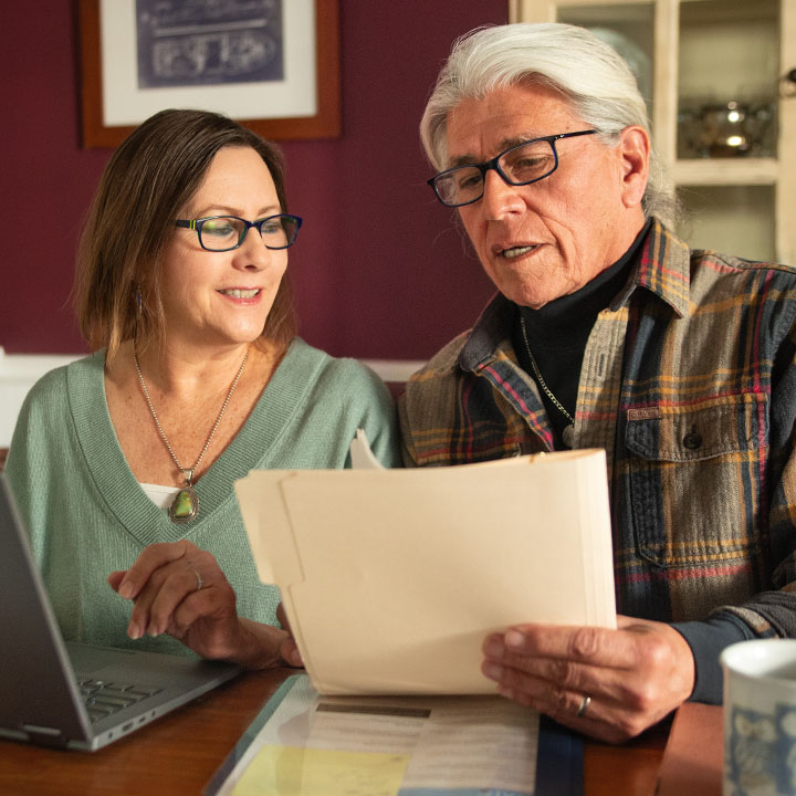 A husband and wife, seated in their home office, review their TruStage Policy Information with their online account.