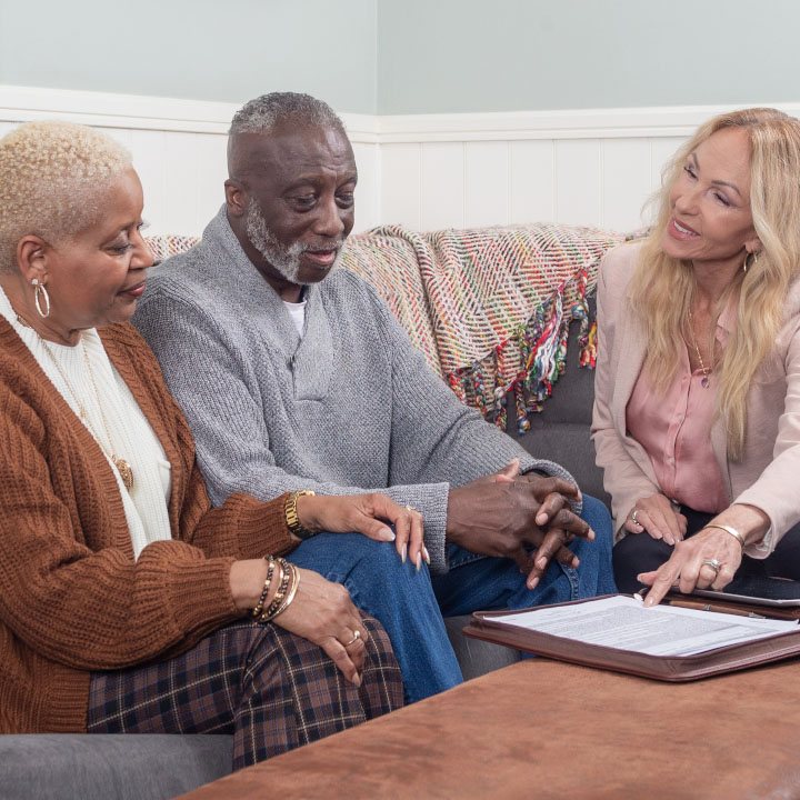 A husband and wife sit on a couch with their insurance agent, who is explaining term life insurance.