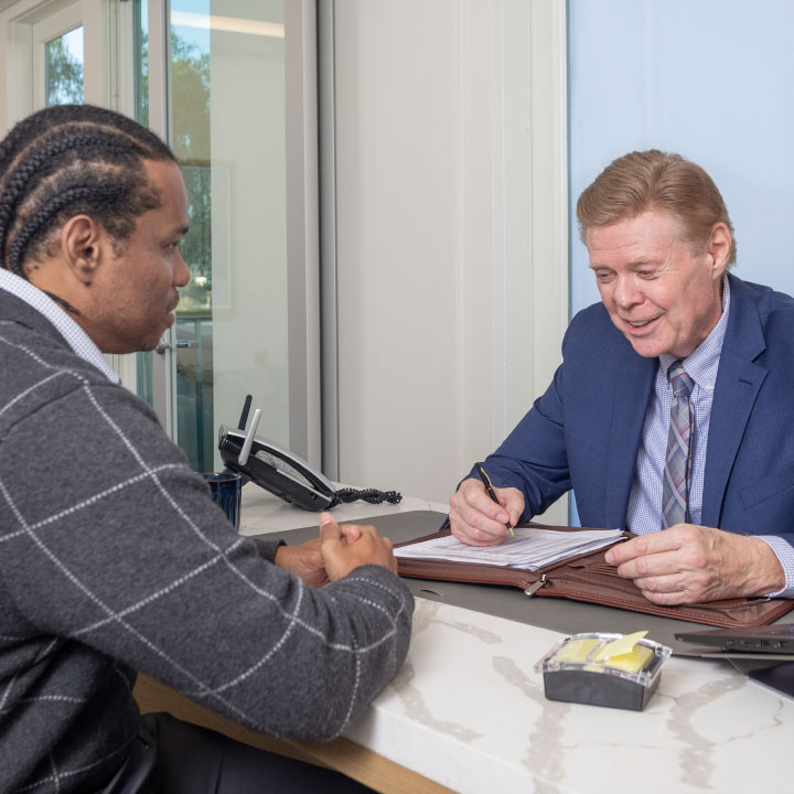 A man sits across a desk from a financial professional who is explaining credit-based insurance scores.