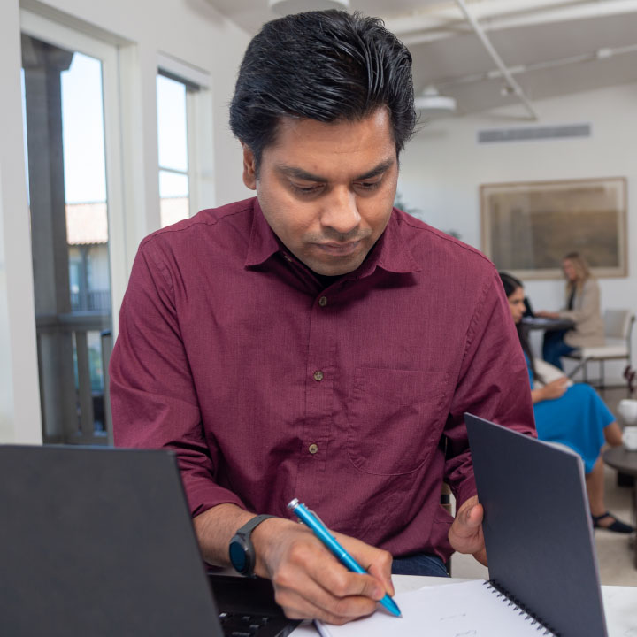 A man sits at a table and writes down notes on electric vehicles and auto insurance.