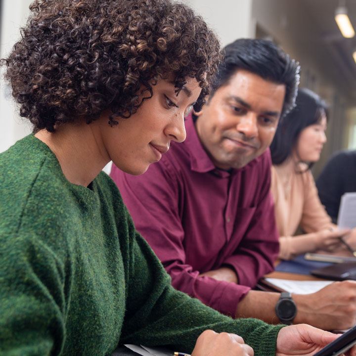 A woman sitting at a desk scrolls on her phone to change a password to an online account.