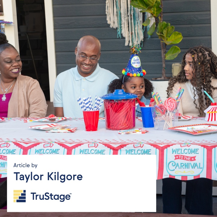 A family sits at a picnic table to celebrate a child's birthday party.