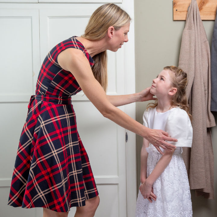 A mother smiles as she helps her daughter get ready to leave the house.