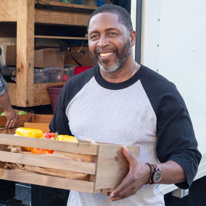 A man unloading a truck carries a crate of vegetables is protected by TruStage Insurance.
