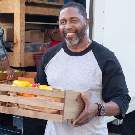 A man unloading a truck carries a crate of vegetables is protected by TruStage Insurance.