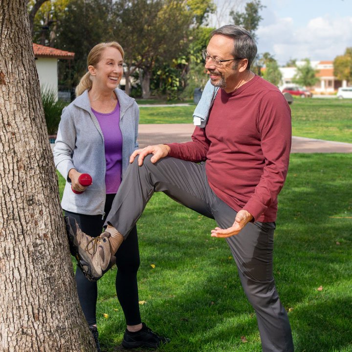 A woman and man discuss life insurance from TruStage while stretching in a park after their workout.