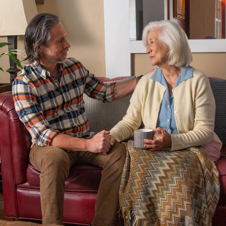 An older son on a couch with his mom discuss her TruStage Life Insurance Policy.