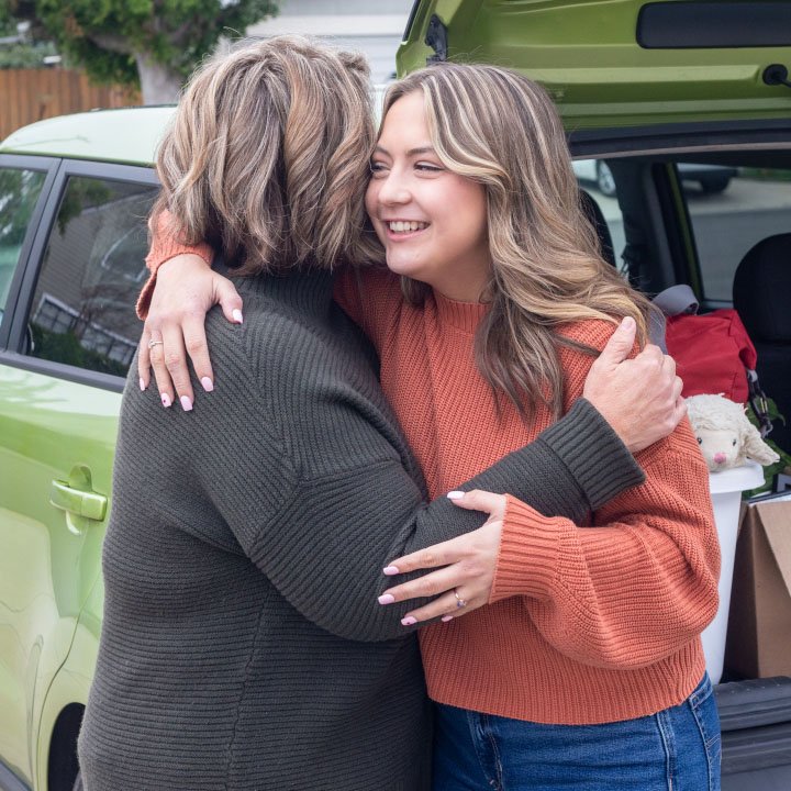 A daughter and mother hug outside a car that is better protected by the TruStage Auto and Home Program