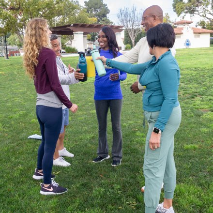 A group of TruStage insured friends working out in a park clank their water bottles together.