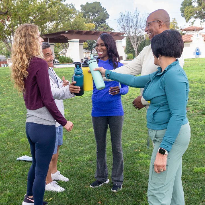 A group of TruStage insured friends working out in a park clank their water bottles together