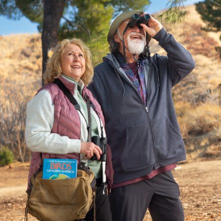 An older couple better protected by TruStage Insurance are birdwatching in the hills.