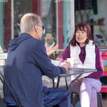 A retired couple at an outdoor cafe drinking coffee are discussing their TruStage Life Insurance policy.