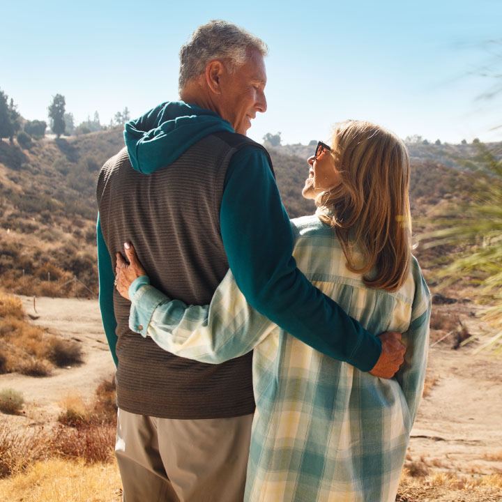 A husband and wife embrace each other, discussing their finances while hiking in the desert.