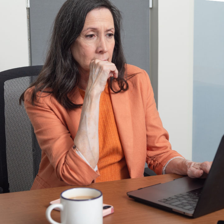 A woman uses a laptop while sitting at a desk to research if she should lease or buy a new car.