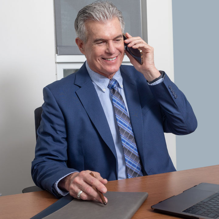 A financial professional sits at a desk and uses a phone to discuss life insurance with a client.