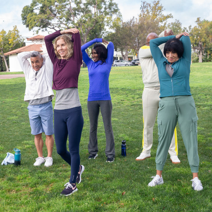 Three women and two men stretch in the park while discussing the importance of budgeting.