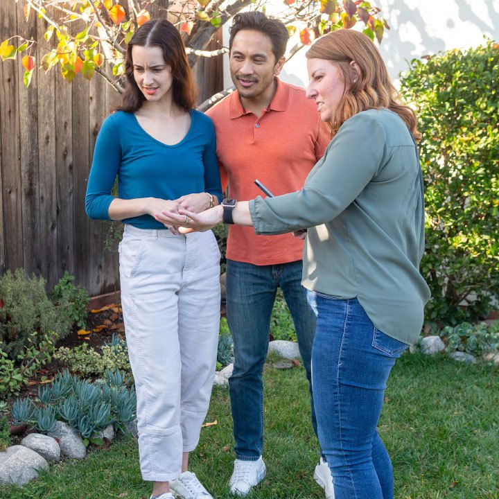 A husband and wife stand with their insurance agent in their yard as she explains homeowner's insurance.