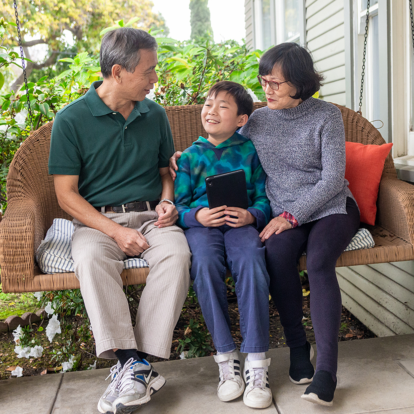 A family of three protected by life insurance enjoys time outside on a porch swing.