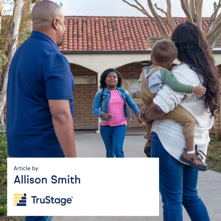 A mother holds a baby next to her husband as they wait to pick up their daughter from school.