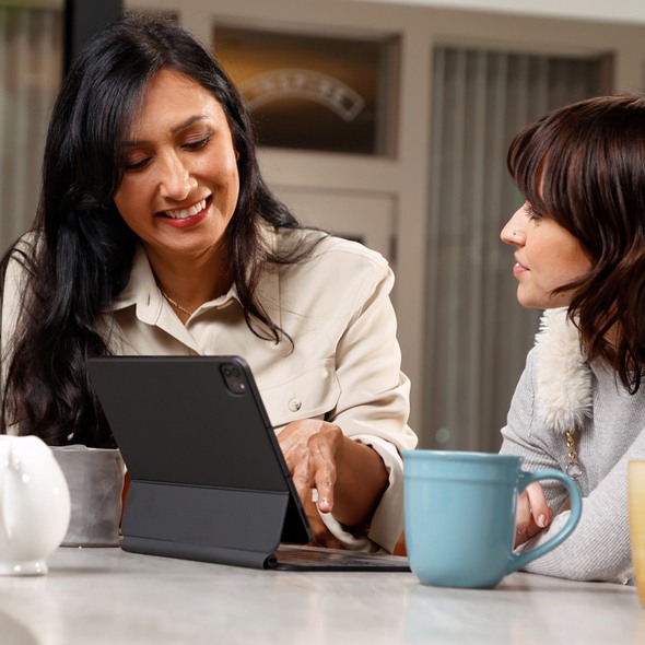 One woman introduces another to TruStage financial solutions on her notebook while having a cup of coffee 