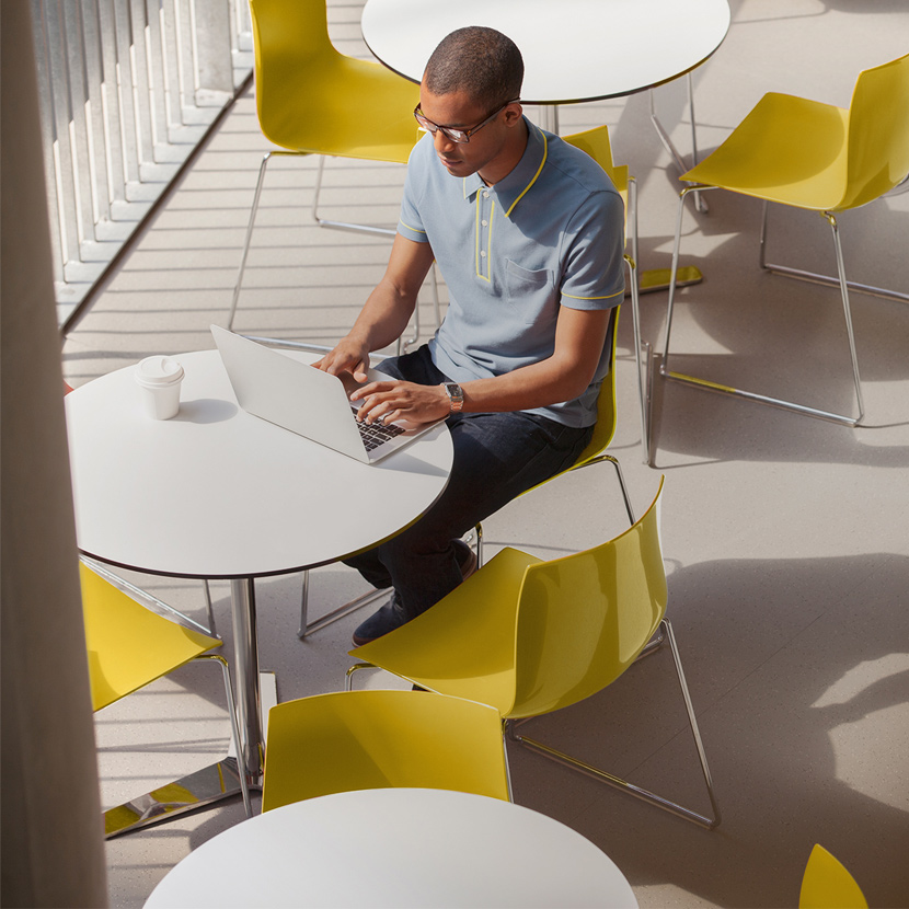 Person using laptop sitting at a table with yellow chairs