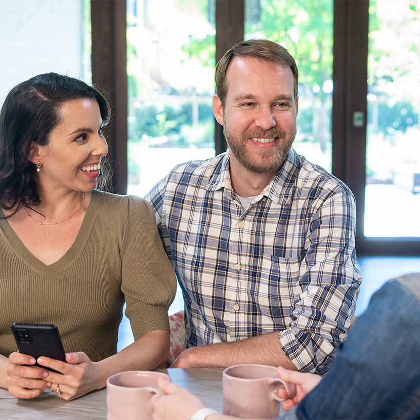 A man and a woman holding a phone sitting at a table smiling